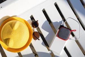 el altavoz portátil de música se carga desde el banco de energía a través de usb en una tumbona cerca de la piscina con accesorios de playa. siempre en contacto, dispositivos de viaje, batería externa para un teléfono inteligente. lugar para el texto. foto