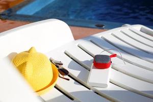 Music portable speaker is charged from the power bank via usb on a deck chair near the pool with beach accessories. Always in touch, travel gadgets, external battery for a smartphone. Place for text. photo