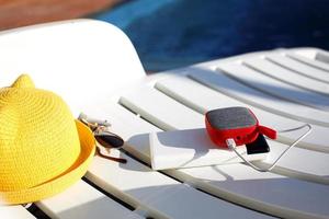 el altavoz portátil de música se carga desde el banco de energía a través de usb en una tumbona cerca de la piscina con accesorios de playa. siempre en contacto, dispositivos de viaje, batería externa para un teléfono inteligente. lugar para el texto. foto