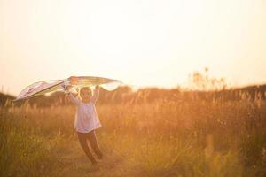una niña corre a un campo con una cometa, aprende a lanzarla. animación al aire libre en verano, naturaleza y aire puro. infancia, libertad y despreocupación. un niño con alas es un sueño y una esperanza. foto