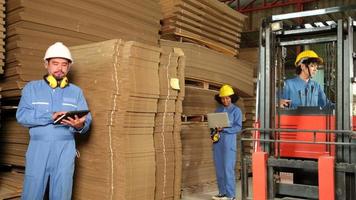 Industry factory workers team in safety uniform and hard hat inspect storage by laptop, stock order at warehouse, management piles of stacking cardboard with a forklift, manufacture product logistic.