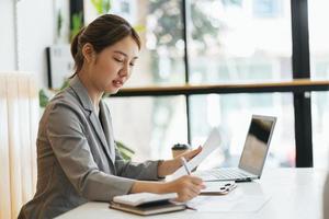 feliz joven mujer asiática sentada y usando una computadora portátil en la sala de estar trabajando desde el concepto de casa foto