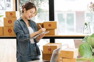 emprendedor de pequeñas empresas, autónomo, retrato de mujer joven que trabaja en la oficina en casa, caja, teléfono inteligente, computadora portátil, en línea, marketing, empaque, entrega, pyme, concepto de comercio electrónico foto