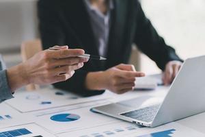 Close up of hands of two men and woman wearing casual clothes working with graphs at a white table and making notes. Locked down real time close up shot photo