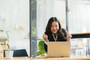 Excited Asian woman sit at desk feel euphoric win online lottery, happy black woman overjoyed get mail at laptop being promoted at work, biracial girl amazed read good news at computer photo