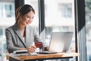 mujer asiática comprando en internet haciendo transacciones de pago instantáneas en la computadora usando tarjeta de crédito. foto