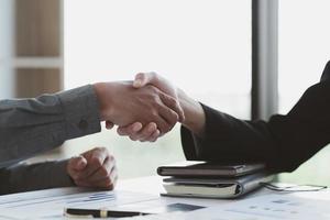 Close up of female and male shaking hands, businessman and businesswoman handshaking above office table with charts graphs after successful negotiations, partners concluding contract, top view