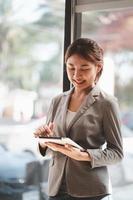 Attractive businesswoman using a digital tablet while standing in front of windows in an office building overlooking the city photo