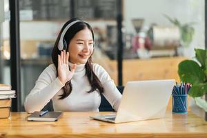 Smiling woman wearing wireless headphones working typing on notebook sit at desk in office workplace. Enjoy e-learning process, easy comfortable application usage, listen music during workday concept