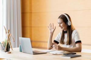 Smiling Asian young female using headset looking at laptop screen listen and learning online courses. Happy chinese business woman with headphones video call for customer service photo