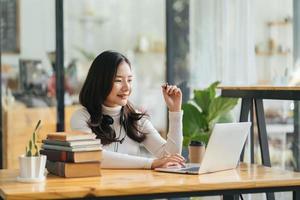 Side vire of happy pretty woman with dark curly hair having video call from home, using headset and laptop in living room, talking to friends or relatives, copy space photo