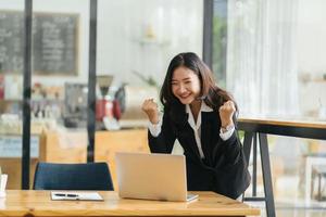 Excited Asian woman sit at desk feel euphoric win online lottery, happy black woman overjoyed get mail at laptop being promoted at work, biracial girl amazed read good news at computer photo