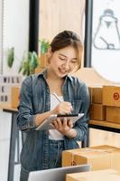 Worker In Warehouse Checking Boxes Using Digital Tablet.Start up small business entrepreneur SME or freelance woman working at home concept, Young Asian small business owner,online marketing.