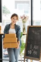una mujer asiática inicia una pequeña empresa propietaria de una caja de cartón en el lugar de trabajo. una vendedora independiente prepara una caja de paquetes de productos para entregar al cliente. venta en línea, comercio electrónico.
