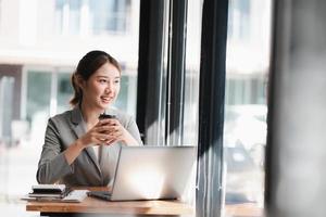 Happy attractive Asian business woman working with a laptop and financial document at office, successful action, Business concept. photo