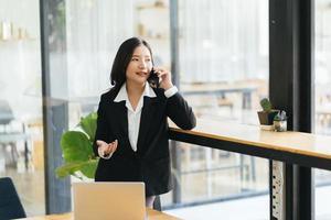 Portrait of young business woman with suit in cafe in front of her laptop and talking on mobile phone photo