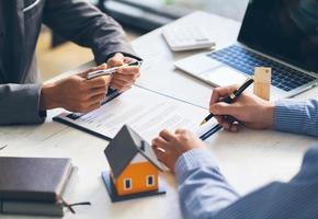 real estate agent assisting client to sign contract paper at desk with house model, house agency and insurance concept. photo