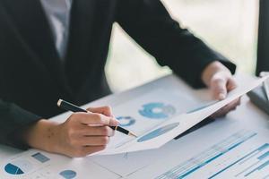 Hand of a businesswoman point analysis financial paper charts and graph on working desk. photo