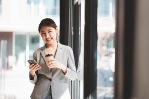 Smiling woman in casuals standing in office. Businesswoman with mobile phone in hand looking at camera. photo