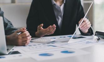 Close up of hands of two men and woman wearing casual clothes working with graphs at a white table and making notes. Locked down real time close up shot photo