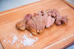 Grilled beef steak was sliced and put on a wooden chopping board with salt. photo