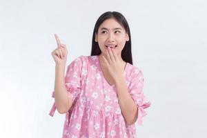 Asian woman in pink dress acts exciting and point up to present something on white background. photo