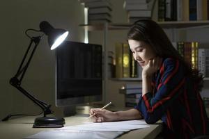 Asian woman working at home in night by using computer to search online information. photo