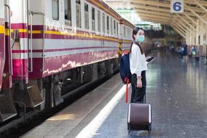 mujer asiática arrastra su bolso para viajar o volver a casa en tren en la estación mientras usa mascarilla médica como nuevo estilo de vida normal en el concepto de atención médica foto