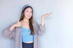 Beautiful young Asian woman is acting thumb up as a good symbol and another hand shows as presenting something on the background.
