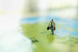 Business Trip and Travel Concept. Close up of businessman miniature figure with handbag suitcase running on colorful world map with copy space.