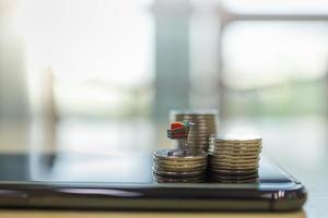 Business E-Commerce and Money Concept. Close up of shopping cart or trolley miniature figure on top of stack of coins on top on smart mobile phone with copy space. photo