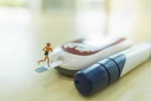 Medicine, diabetes, glycemia, health care and people concept - close up of woman runner miniature figure running on blood sugar test strip and connect to Glucose meter on wooden table. photo