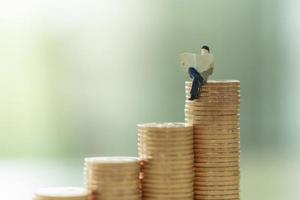 Money, Business, Saving and Planning concept. Close up of businessman miniature figure perople sitting and reading a newspaper on stack of gold coins with copy space. photo