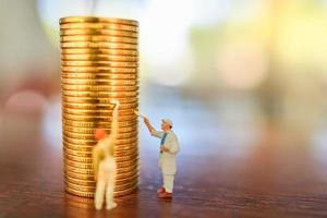 Business, Money, Planning and Saving Concept. Close up of group of worker cleaning and painting stack of gold coin on wooden table with copy space. photo