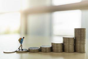 Travel, Saving and planning Concept. Close up of traveler miniature figure people with backpack walking on top of stack of coins with copy space. photo