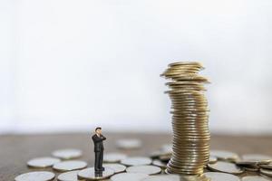 Business, Risk, Investment and Saving Concept.  Close up of businessman miniature people figure standing and looking to unstable stack of coins with copy space. photo