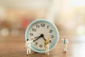 Time management concept. Close up of group of worker miniature people figures clean and paint vintage round clock on wooden table. photo