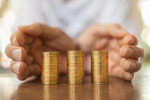 Business, Money, Finance, Saving and Security Concept. Close up of man hands protect three stack of gold coins on wooden table. photo