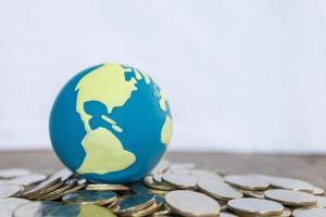 Global Business and Financial Concept. Close up of world mini ball on pile of coins on wooden table and copy space. photo
