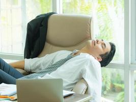 joven empresario asiático cansado y durmiendo después de encontrar información en Internet, para usar en la competencia empresarial foto