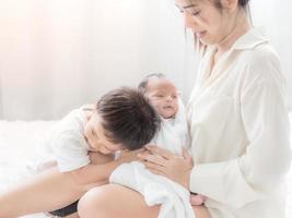 A beautiful Asian woman holds her newborn daughter and her son hugs his sister with love as well photo