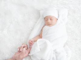 Newborn baby girl sleeps warmly on the white cloth and touched her father's hand with love