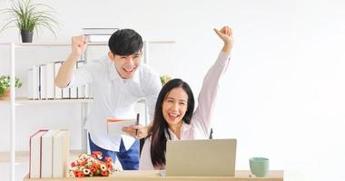 pareja asiática celebrando su nueva venta alta después de usar una computadora portátil para una subasta en línea mientras trabajaba desde casa para una nueva política normal con espacio para copiar
