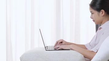 asiatisk kvinna som arbetar med bärbar dator i mysigt sovrum med vit gardin på bakgrunden, arbeta hemifrån isolering, frilansande författare skriver inspiration, färska idéer på morgonen, arbeta ensam video