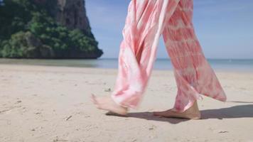 Young beautiful lady walking on the island windy beach, wind blowing clothes in slow motion. Vacation travel destination paradise on earth, relaxing beach walking scene. summer fashion beach wear video