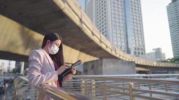 atractiva mujer de negocios apoyada en un pasamanos de metal en un puente peatonal con la mano usando una tableta digital, un dispositivo inalámbrico conveniente para trabajar al aire libre, una innovación tecnológica de trabajo en línea video