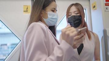 en ung elegans asiatiska affärskvinnor bär ansiktsmask pratar och tittar på telefonen på det allmänna tåget, andningsskydd på covid-19-pandemin, femininitetssamhälle, rusningstid, arbetsförberedelser video