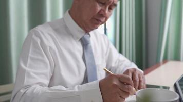 hombre asiático de mediana edad trabajando desde casa, escribiendo información importante en el cuaderno, concentrándose en el trabajo, trabajando en casa durante el encierro, traje de negocios con corbata, hombre estresante video