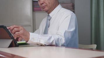 Asian Business man working from home office with wireless tablet, writing down on notebook, concentrate focus on work, working at home during lockdown, necktie business attire clothing, online meeting video