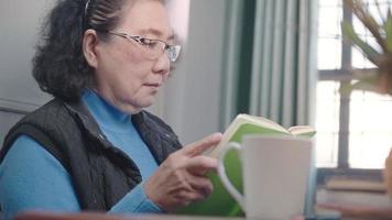Senior Asian grandma read book inside cozy home Livingroom table, relaxation vibe, old age learning, leisure relaxation, happy retirement life, staying at home in self isolation in quarantine lockdown video